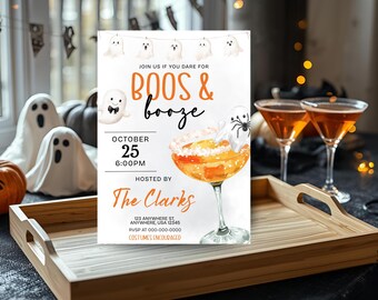May include: A Halloween-themed invitation with the text "Boos & Booze" and event details. The invitation features a cocktail illustration with a ghost and spider, along with decorative ghost figures and pumpkins. The invitation is on a wooden tray with two martini glasses.