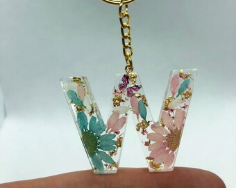 May include: A gold key chain with a resin letter W charm. The letter is filled with pressed flowers and gold leaf.