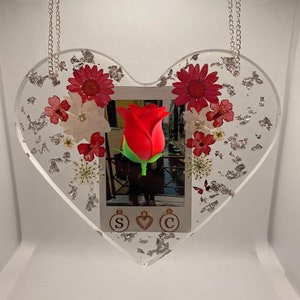 May include: A heart-shaped resin ornament with a silver chain, featuring a red rose, dried flowers, and silver leaf accents. The ornament also includes a photo with the letters "S", a heart, and "C" hanging from it.