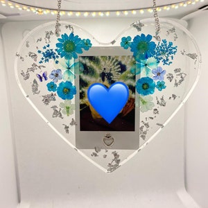 May include: A heart-shaped resin ornament with a silver chain, featuring pressed blue flowers and silver leaf accents. A small photo is encased in the center, with a blue heart overlayed on the image.