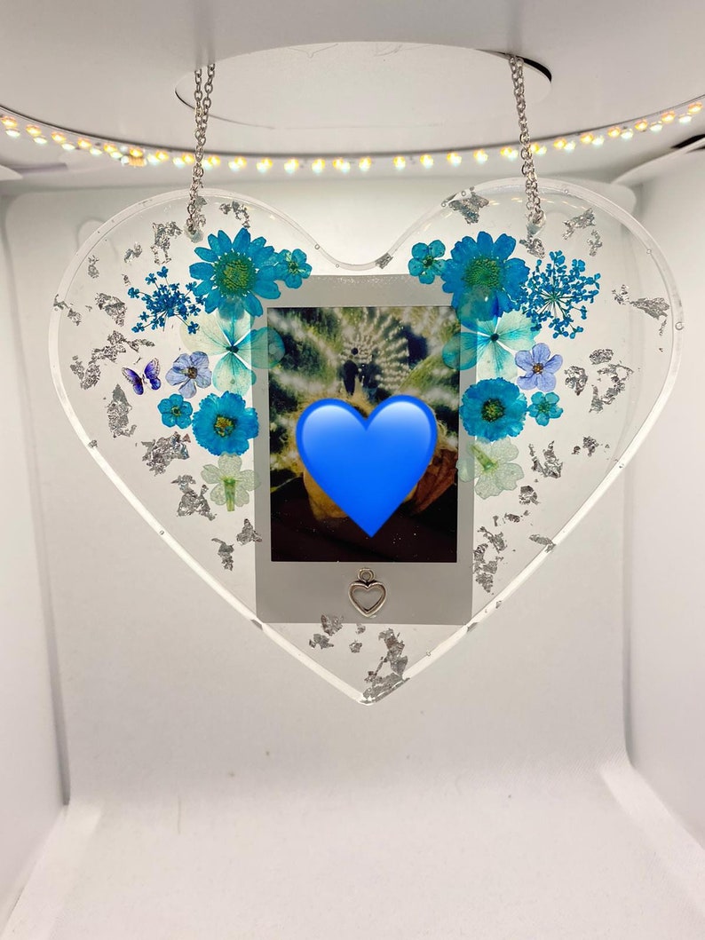 May include: A heart-shaped resin ornament with a silver chain, featuring pressed blue flowers and silver leaf accents. A small photo is encased in the center, with a blue heart overlayed on the image.