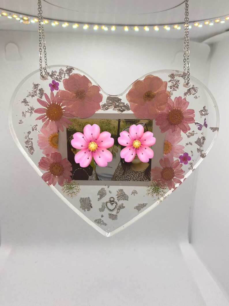 May include: A heart-shaped resin picture frame with a photo of two people and pressed flowers. The frame is hanging from a silver chain and has a silver heart charm.