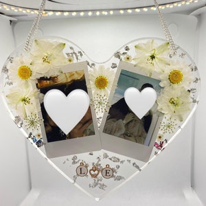 May include: A white heart-shaped resin ornament with two Polaroid photos, white flowers, silver glitter, and gold charms with the letters "L" and "E".