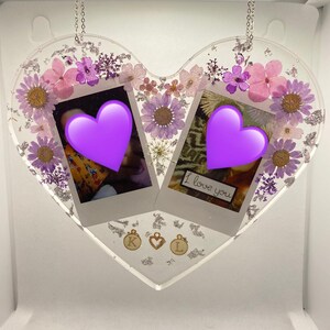 May include: A heart-shaped resin ornament with pressed flowers and two photo frames. The frames contain photos with purple hearts and the text "I love you". The ornament is hanging from a silver chain and has gold charms with the letters "K" and "L" and a heart.