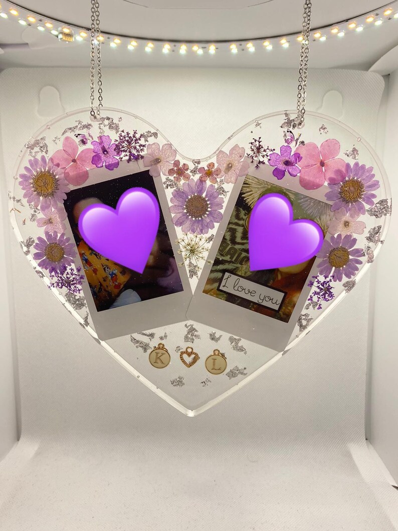 May include: A heart-shaped resin ornament with pressed flowers and two photo frames. The frames contain photos with purple hearts and the text "I love you". The ornament is hanging from a silver chain and has gold charms with the letters "K" and "L" and a heart.