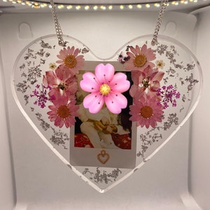 May include: A heart-shaped resin ornament with a photo of two children and pressed flowers. The ornament is hanging from a silver chain.