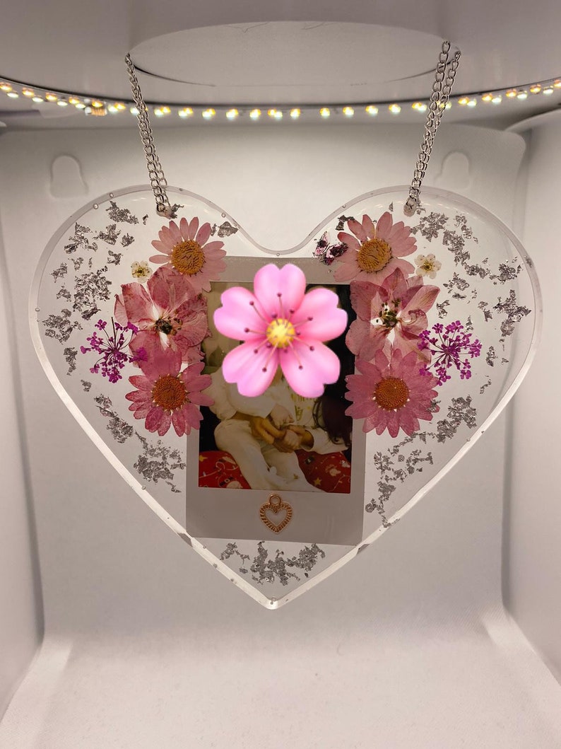 May include: A heart-shaped resin ornament with a photo of two children and pressed flowers. The ornament is hanging from a silver chain.
