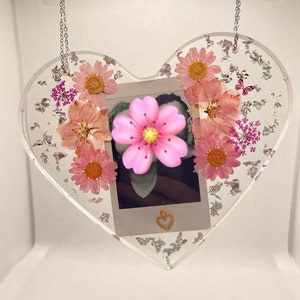 May include: A heart-shaped resin ornament with a silver chain, featuring pressed flowers and a small photo inside. The ornament is decorated with silver glitter.