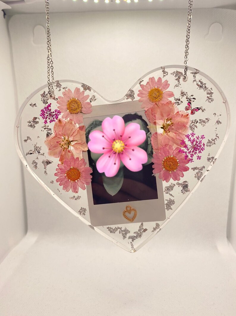 May include: A heart-shaped resin ornament with a silver chain, featuring pressed flowers and a small photo inside. The ornament is decorated with silver glitter.