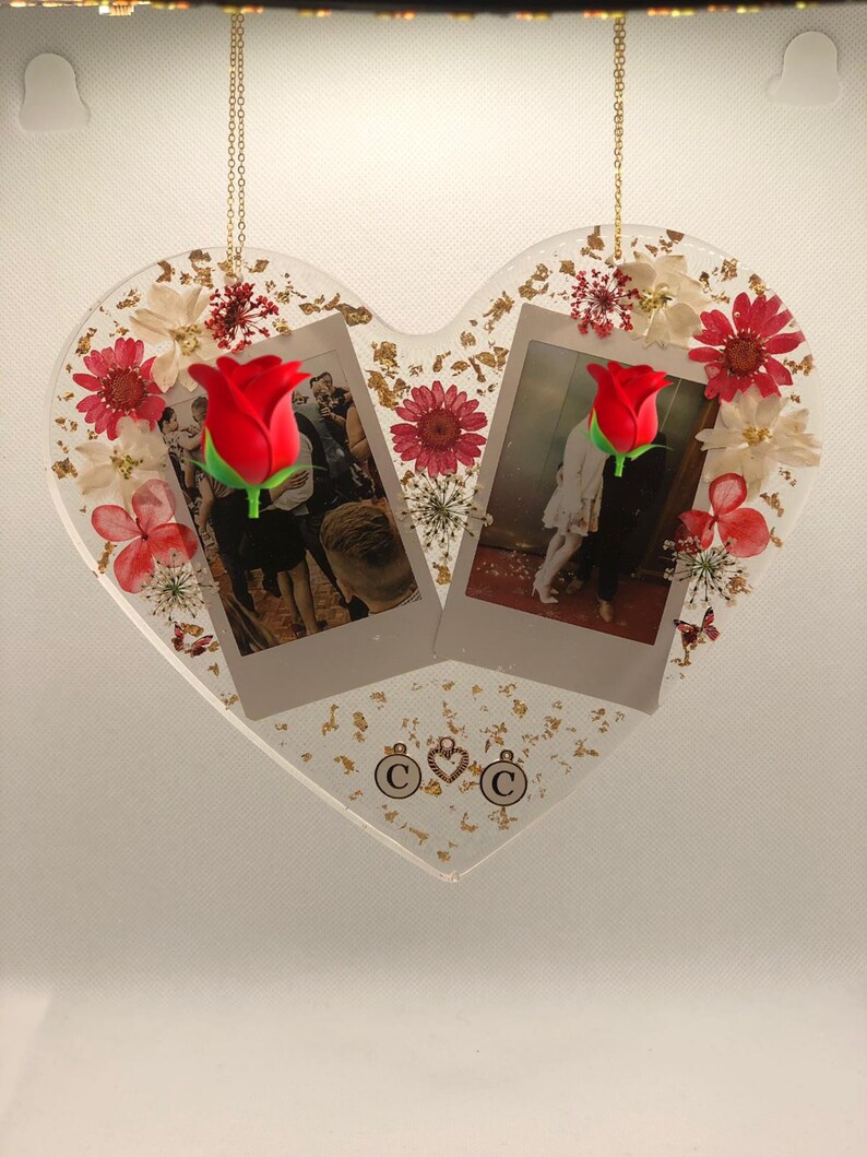 May include: A heart-shaped resin ornament with two framed photos, dried flowers, and gold leaf accents. The photos feature a couple and a red rose. The ornament has two charms with the letter "C" and a heart.