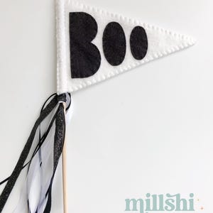 May include: White felt pennant with black felt letters spelling "BOO" on a wooden stick with black and white ribbon streamers.