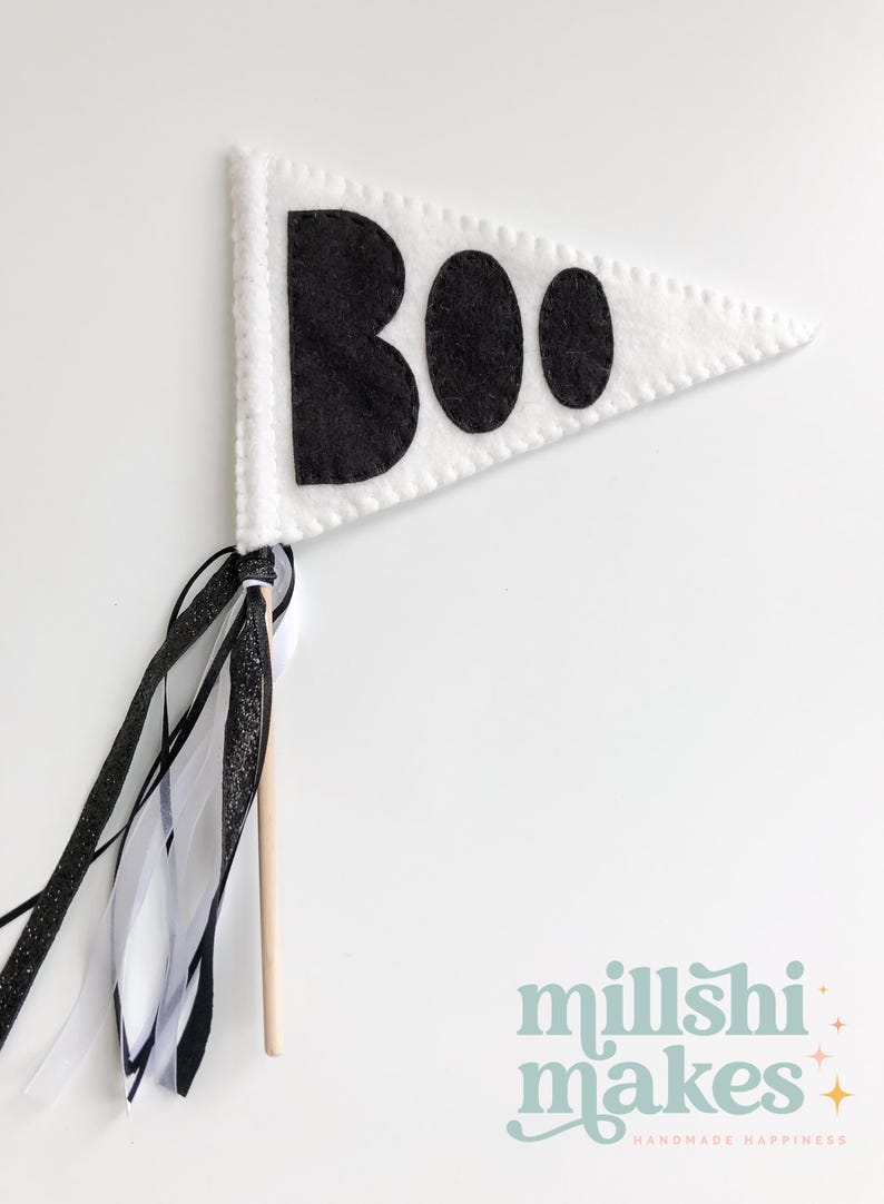 May include: White felt pennant with black felt letters spelling "BOO" on a wooden stick with black and white ribbon streamers.