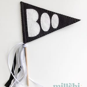 May include: A black felt pennant with white felt letters spelling "BOO" on a wooden stick with black, white, and silver ribbon streamers.