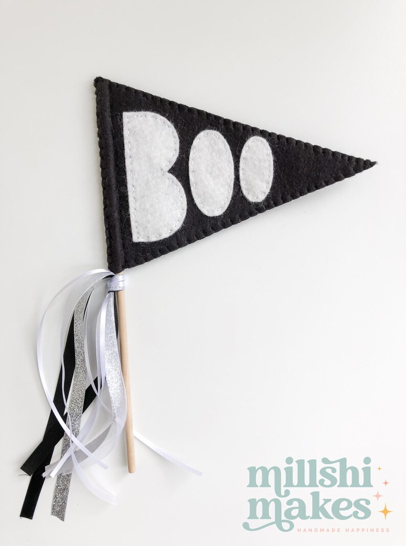 May include: A black felt pennant with white felt letters spelling "BOO" on a wooden stick with black, white, and silver ribbon streamers.
