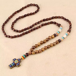 K&ouml;nnte beinhalten: Eine braune Holzperlenkette mit einem Kreuzanh&auml;nger. Das Kreuz ist mit blauen, gr&uuml;nen und roten Akzenten verziert.