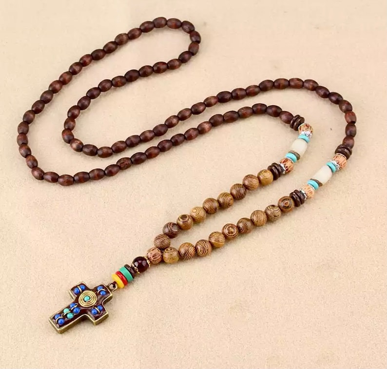 K&ouml;nnte beinhalten: Eine braune Holzperlenkette mit einem Kreuzanh&auml;nger. Das Kreuz ist mit blauen, gr&uuml;nen und roten Akzenten verziert.