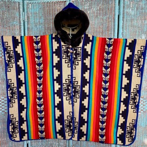 May include: A vibrant poncho with a blue hood and faux fur trim. The poncho displays a geometric pattern in cream, navy, red, orange, yellow, and turquoise stripes. The edges are trimmed in blue.