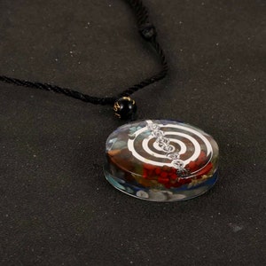 K&ouml;nnte beinhalten: Eine Halskette mit einem klaren Kristall-Anh&auml;nger, der ein silberfarbenes Spiralmuster und verschiedene farbige Steine ​​im Inneren aufweist. Die Halskette ist an einem schwarzen Band.