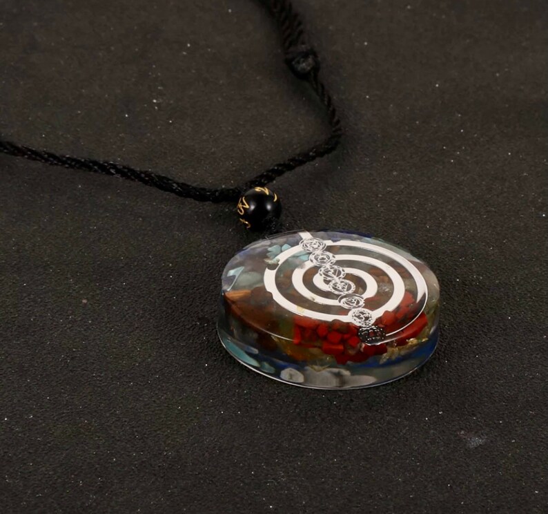 K&ouml;nnte beinhalten: Eine Halskette mit einem klaren Kristall-Anh&auml;nger, der ein silberfarbenes Spiralmuster und verschiedene farbige Steine ​​im Inneren aufweist. Die Halskette ist an einem schwarzen Band.