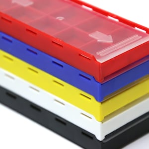 May include: A stack of five plastic storage boxes with lids. The boxes are red, blue, yellow, white, and black. The boxes have a clear plastic lid with an arrow pointing down.