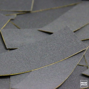 May include: Close-up of a stack of black grip tape sheets with yellow edges. The sheets are textured and have a rough surface.