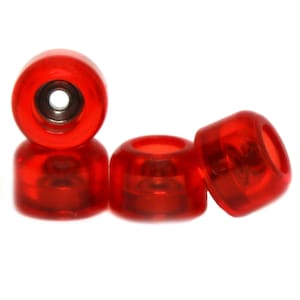 Puede incluir: Cuatro ruedas de fingerboard rojas. Las ruedas son de plástico transparente y tienen un tinte rojo. Las ruedas están dispuestas en fila, con las dos ruedas exteriores ligeramente inclinadas.
