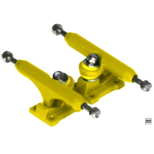 May include: A pair of yellow fingerboard trucks with silver axles and black hardware. The trucks are designed for fingerboards, which are miniature skateboards.