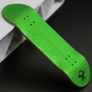 May include: A green fingerboard with black grip tape and a black alien graphic. The fingerboard is made of wood and has a rounded shape.