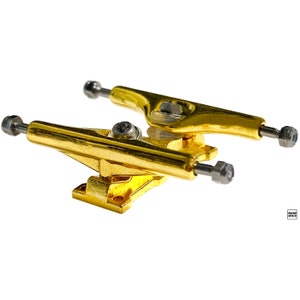 May include: Gold-coloured fingerboard trucks with silver axles and bolts. The trucks are designed for fingerboards, which are miniature skateboards.