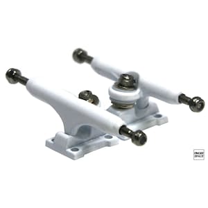 May include: A pair of white fingerboard trucks with silver hardware. The trucks are designed for use with fingerboards, which are miniature skateboards.