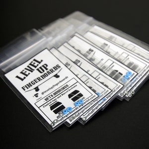 May include: Clear plastic bags containing fingerboard bushings. Each bag has a white label with black text that reads "LEVEL UP FINGERBOARDS" and "BETA BUSHINGS". The labels also show a skateboard graphic and blue bushings.