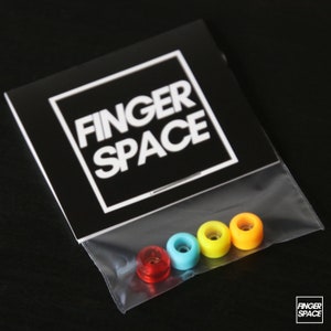 May include: Four fingerboard wheels in a clear plastic bag with a black and white card that says "Finger Space". The wheels are red, blue, yellow, and orange.
