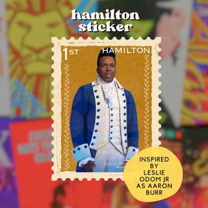 May include: A sticker featuring a portrait of Leslie Odom Jr. as Aaron Burr from the musical Hamilton, designed to resemble a postage stamp. The stamp is bordered in gold and has the text "1st HAMILTON". The sticker is set against a blurred background of other musical posters.