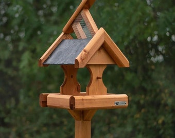 May include: A wooden bird feeder with a slate roof and a wire mesh top. The feeder has two feeding stations and a metal plaque with the text "Wildlife World".