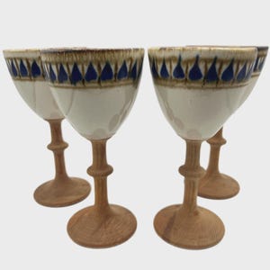 May include: Set of four wine glasses. Each glass features a white bowl with a brown and blue patterned rim, and a wooden stem and base. The glasses are arranged in a group, showcasing their design and craftsmanship.