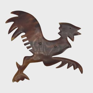 May include: A brown rooster-shaped hair comb. The comb features a detailed design with a stylized rooster silhouette, including a comb section and a decorative tail. The comb is made of a dark brown material with a polished finish.