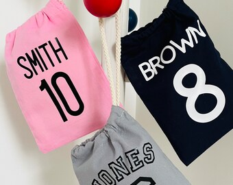 May include: Three drawstring bags with personalized names and numbers. The bags are pink, navy blue, and gray. The names are Smith, Brown, and Jones. The numbers are 10, 8, and 6.