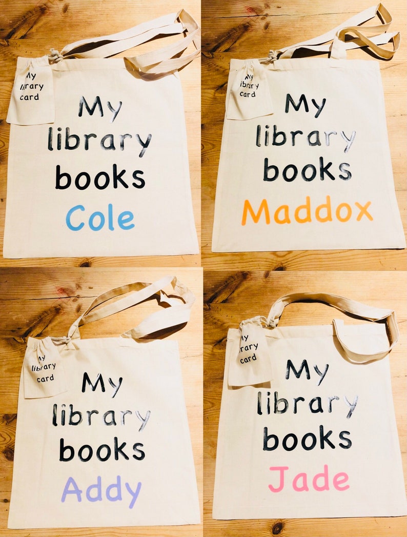 May include: Four canvas tote bags with the text "My library books" in black. Each bag has a different name in a different color: Cole (blue), Maddox (orange), Addy (purple), and Jade (pink). Each bag has a small pocket with "My library card" printed on it.