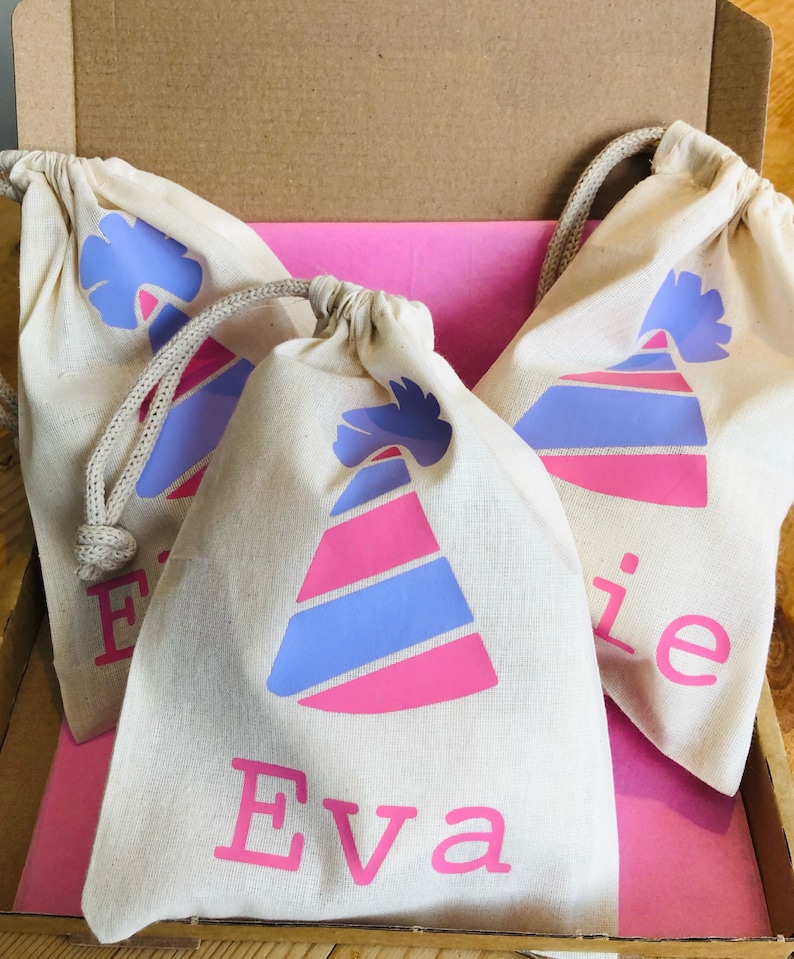May include: Three white cotton drawstring bags with pink and blue party hats and names printed on them. The bags are in a cardboard box with pink tissue paper.