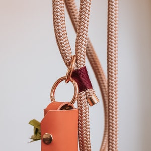 May include: A tan rope dog leash with a matching poop bag holder. The holder is made of orange leather and has a gold snap closure. The leash has a gold clasp and a burgundy accent.