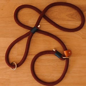 May include: A burgundy rope dog leash with a loop design. The leash features gold-colored metal accents, a dark teal accent, and a small tan leather detail. The leash is designed for easy handling and control.