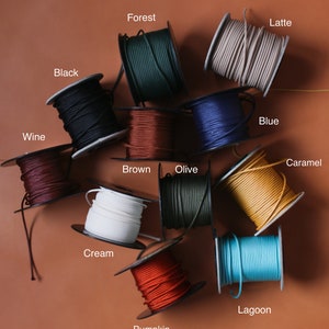 May include: A collection of spools of colorful cord in various shades, including black, forest green, wine, brown, cream, olive, blue, caramel, pumpkin, lagoon, and latte. Each spool is labeled with its color name.