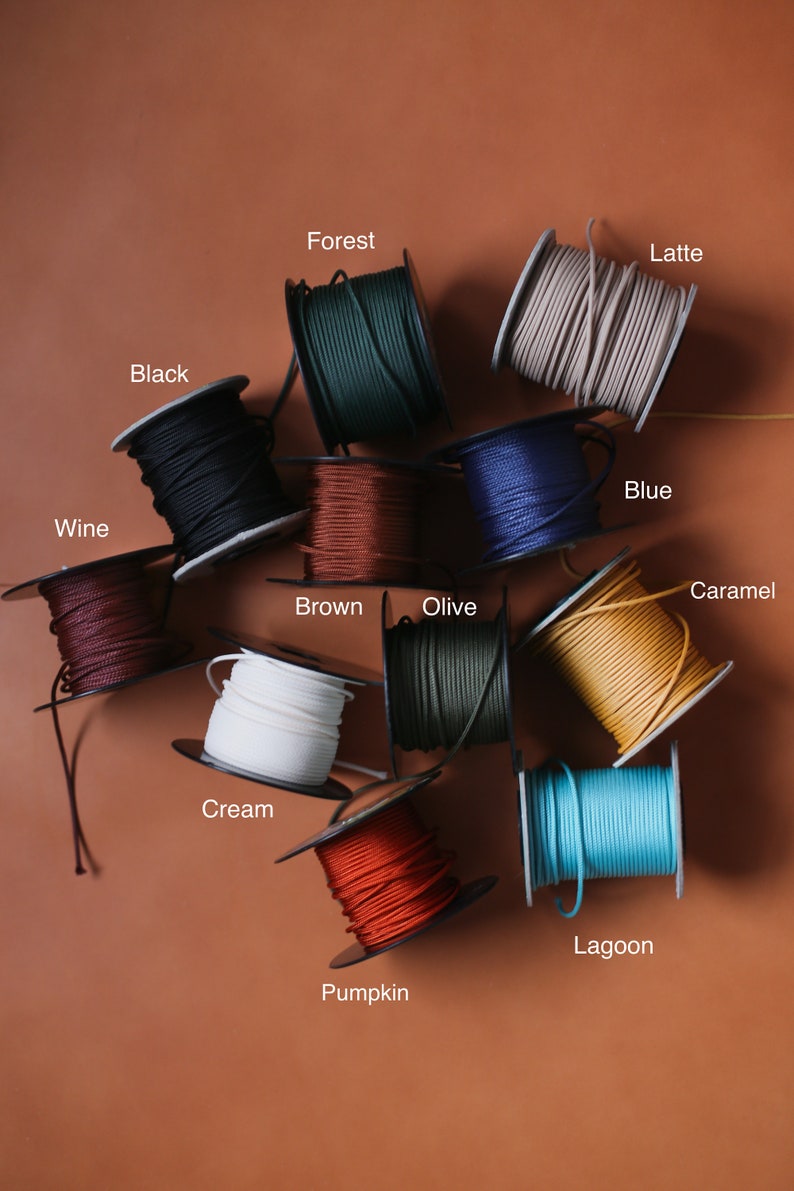 May include: A collection of spools of colorful cord in various shades, including black, forest green, wine, brown, cream, olive, blue, caramel, pumpkin, lagoon, and latte. Each spool is labeled with its color name.