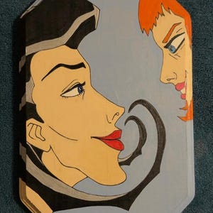 May include: A hand-painted wooden plaque featuring two stylized faces in profile against a light blue background. One face has black hair and red lips, the other has red hair and a sinister expression. The artwork is framed with a dark border.