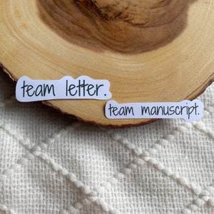 May include: Two white stickers with black handwritten text. The first sticker says "team letter." The second sticker says "team manuscript."