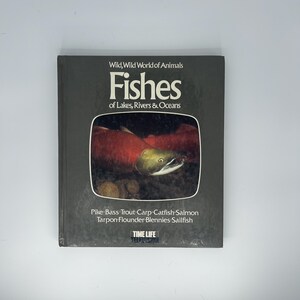 Könnte beinhalten: Ein Hardcover-Buch mit dem Titel "Fishes of Lakes, Rivers & Oceans" aus der Reihe "Wild, Wild World of Animals". Das Cover zeigt ein lebendiges Bild eines Fisches. Das Buch listet verschiedene Fischarten auf, darunter Hecht, Barsch und Lachs.