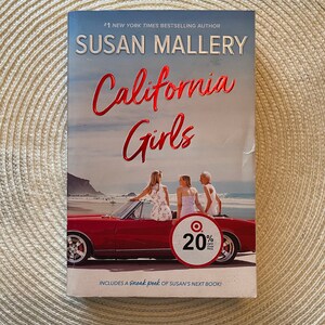 May include: A book cover with a red convertible car and three women standing on the back of the car. The book title is "California Girls" by Susan Mallery. The cover also includes a 20% off Target price tag.