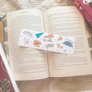 May include: A colorful bookmark with illustrations of a takeout container, a coffee cup, a building with a sign that says "Yale", a gazebo, a sign that says "Antiques", a pizza slice, a telescope, and an umbrella. The bookmark also has the text "I will follow" and "in omnia paratus".