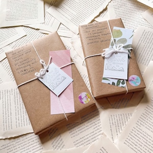 May include: Two wrapped books with tags that read "This Book Belongs To" and "Thank You" stickers. The books are wrapped in brown paper and tied with white twine. One tag has a floral design, and the other has a pink paper backing.