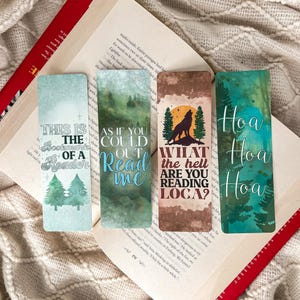 Op de afbeelding: Vier rechthoekige bladwijzers met unieke ontwerpen en tekst. Eén bladwijzer leest "This is the bookmark of a reader" met dennenbomen. Een andere zegt "As if you could read me." De derde heeft een wolfsilhouet en de tekst "What the hell are you reading loca?" De laatste zegt "Hoa Hoa Hoa."